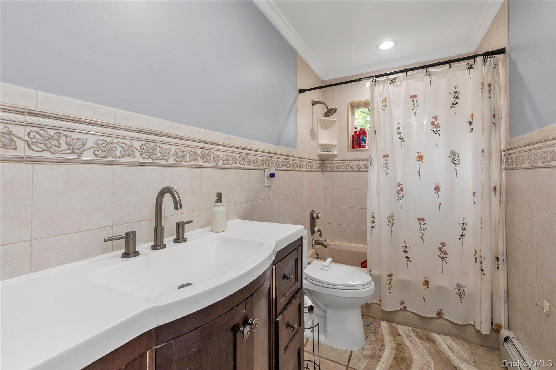 Bathroom featuring a dark wood vanity with an integrated basin, bronze-finish hardware, ceramic wall tiling with decorative floral inlay, and a built-