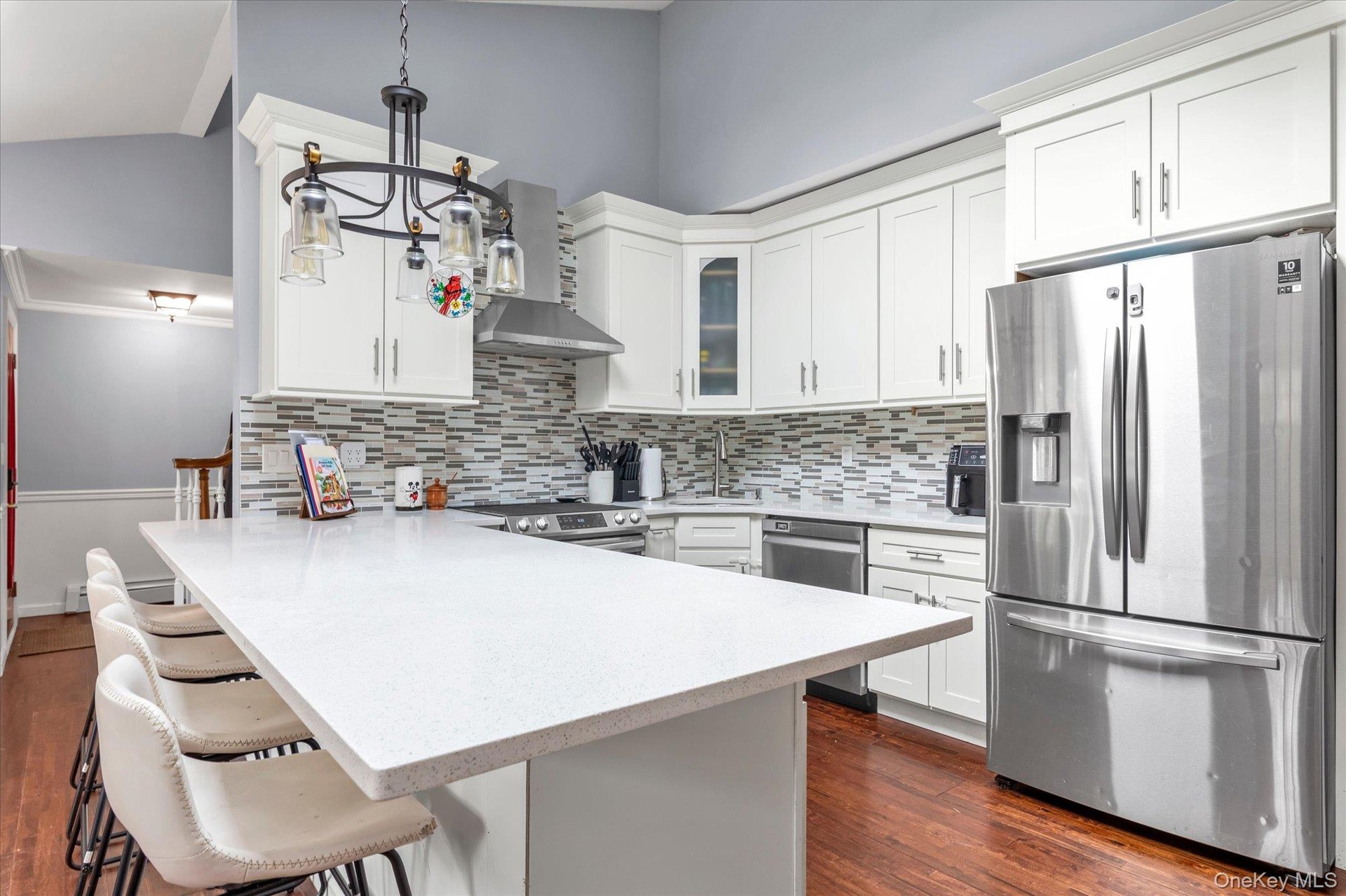 Kitchen featuring white shaker-style cabinetry, quartz countertops, stainless steel appliances, multi-toned tile backsplash, and wood-finish flooring