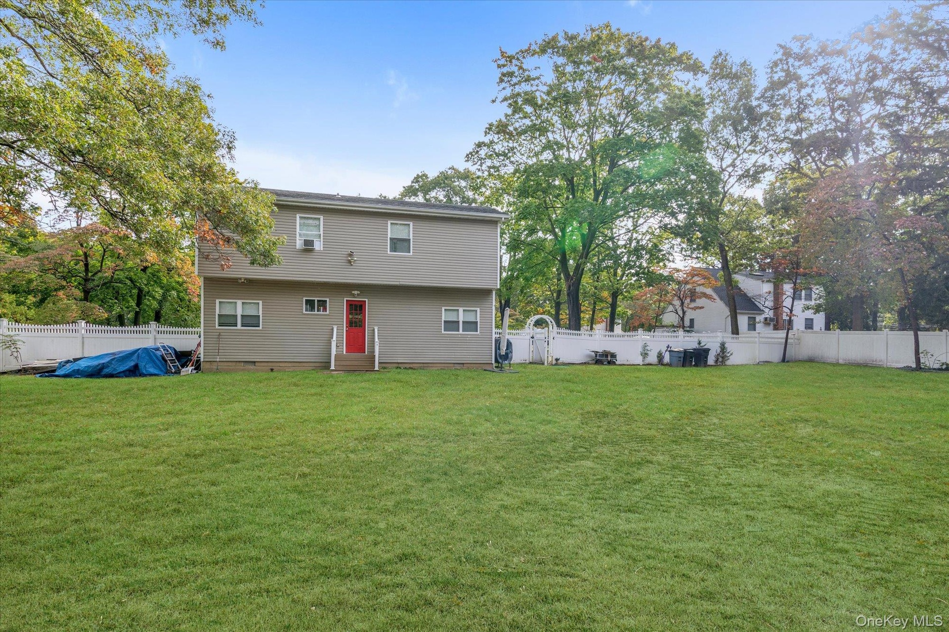 Expansive backyard featuring a level lawn, mature trees, and a white privacy fence