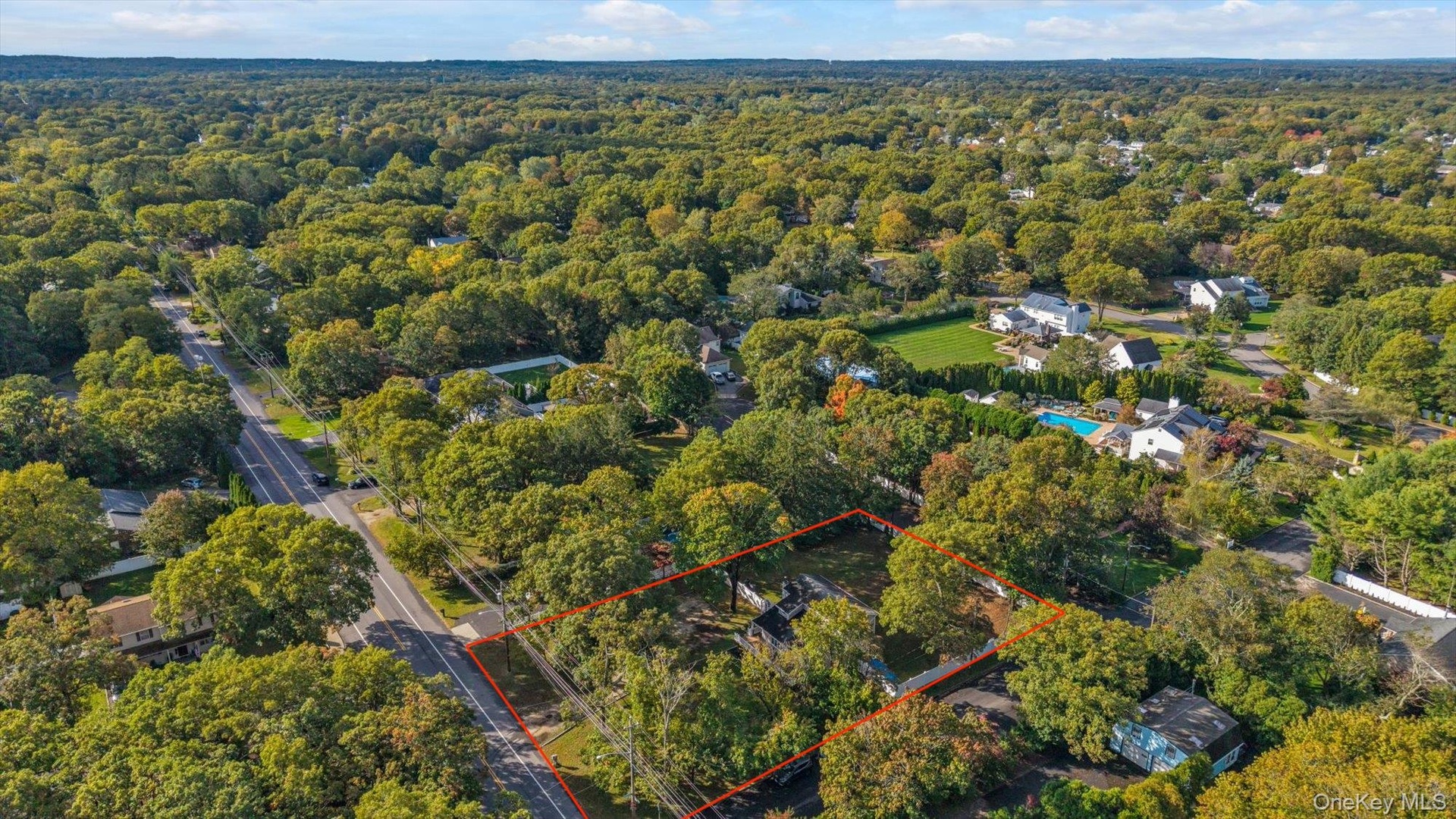 Aerial perspective of a lot featuring mature trees, wooded surroundings, and direct road access