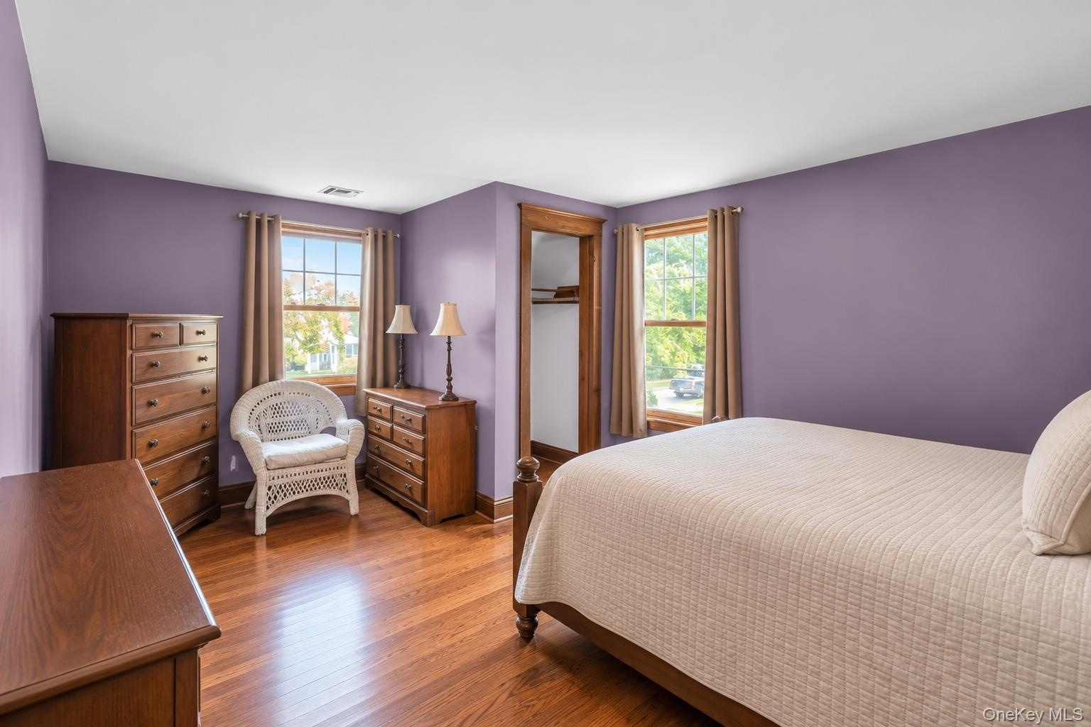 Bedroom featuring wood-finish flooring, two large windows, and a closet with wood trim