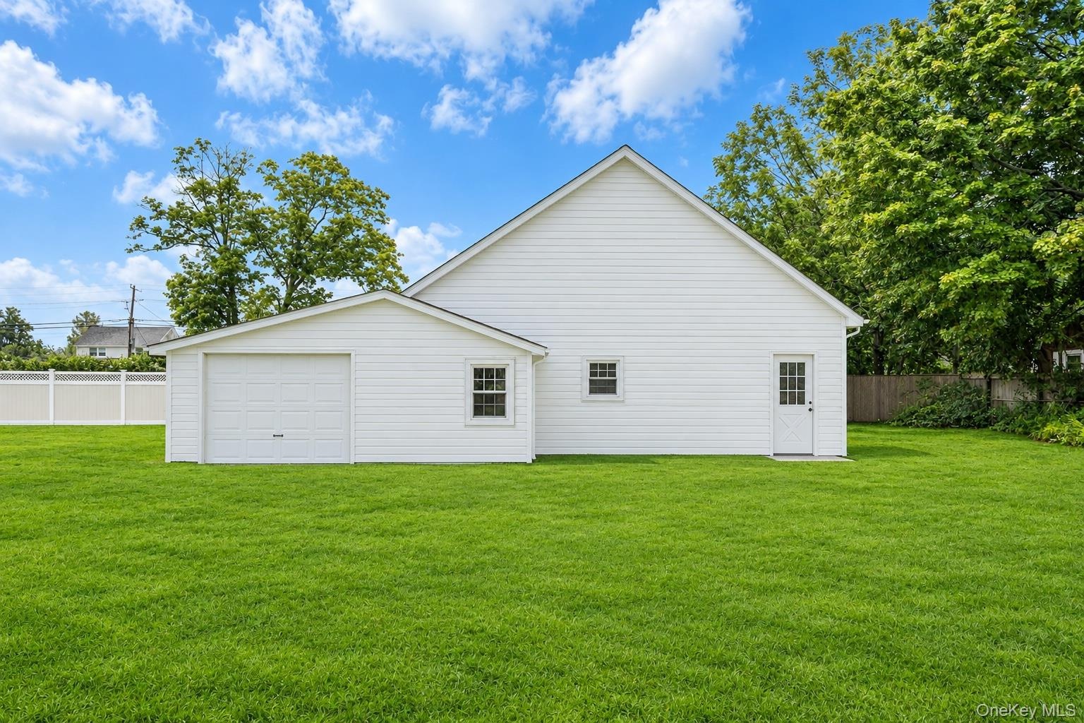 Exterior featuring white horizontal siding, an attached single-bay garage, a separate pedestrian entrance, two windows, and a sprawling grass lawn