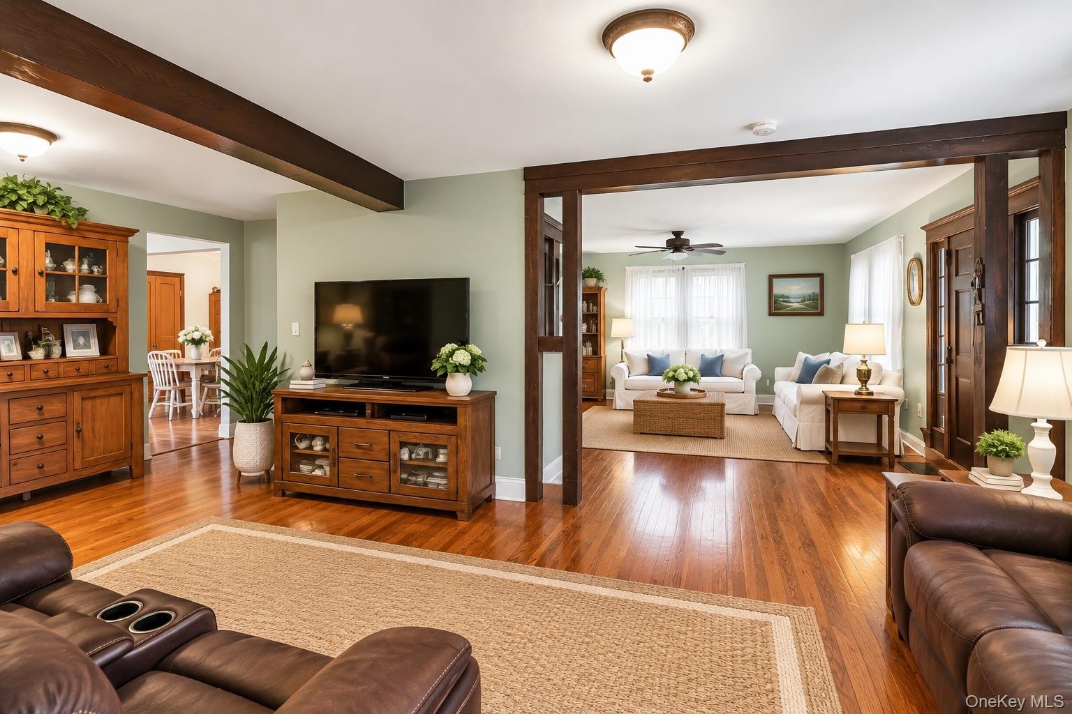 Open-concept living space featuring wood-finish flooring, dark wood crown molding, exposed ceiling beams, and multi-pane windows