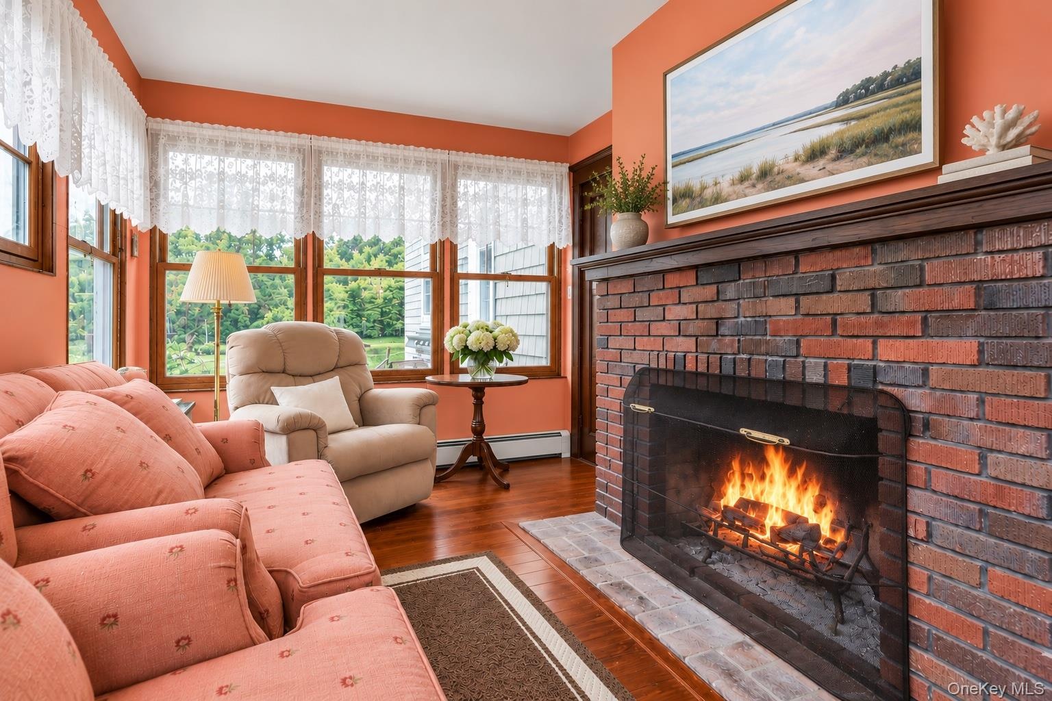 Red brick fireplace with a wood mantel, wood-finish flooring, and multiple windows with wood frames