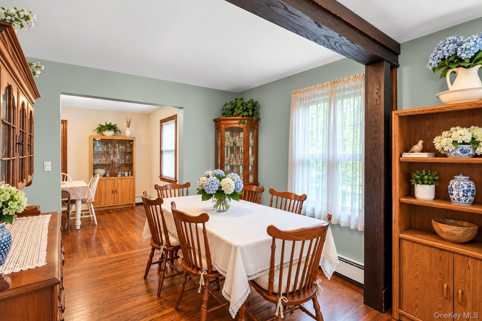 Dining space featuring wood-finish flooring, exposed stained wood structural beam, and natural light through large windows