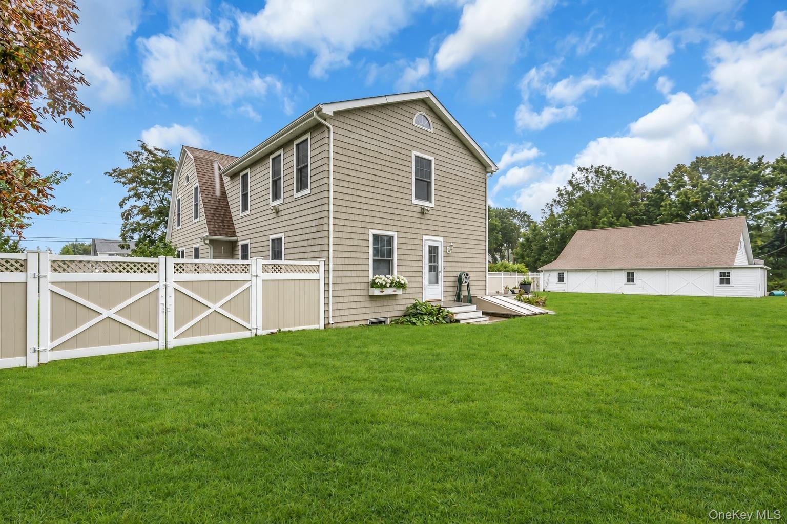 Expansive rear lawn featuring a detached garage, a white vinyl privacy fence with cross-buck detailing, and shingle-style exterior siding