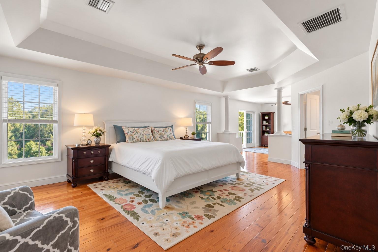 The spacious primary bedroom offers a peaceful private retreat, showcasing gleaming pinewood floors, distinctive tray ceilings with architectural soff