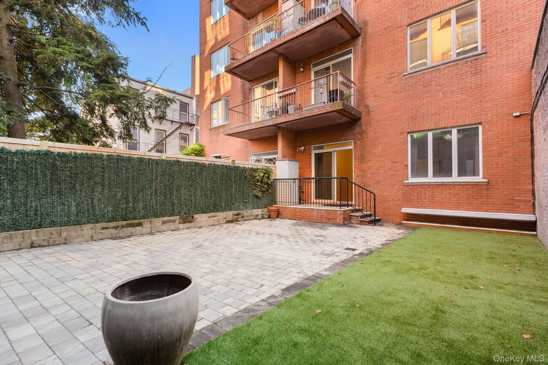 Private patio featuring interlocking stone pavers, synthetic lawn area, perimeter privacy fencing, and exterior staircase access to sliding glass door