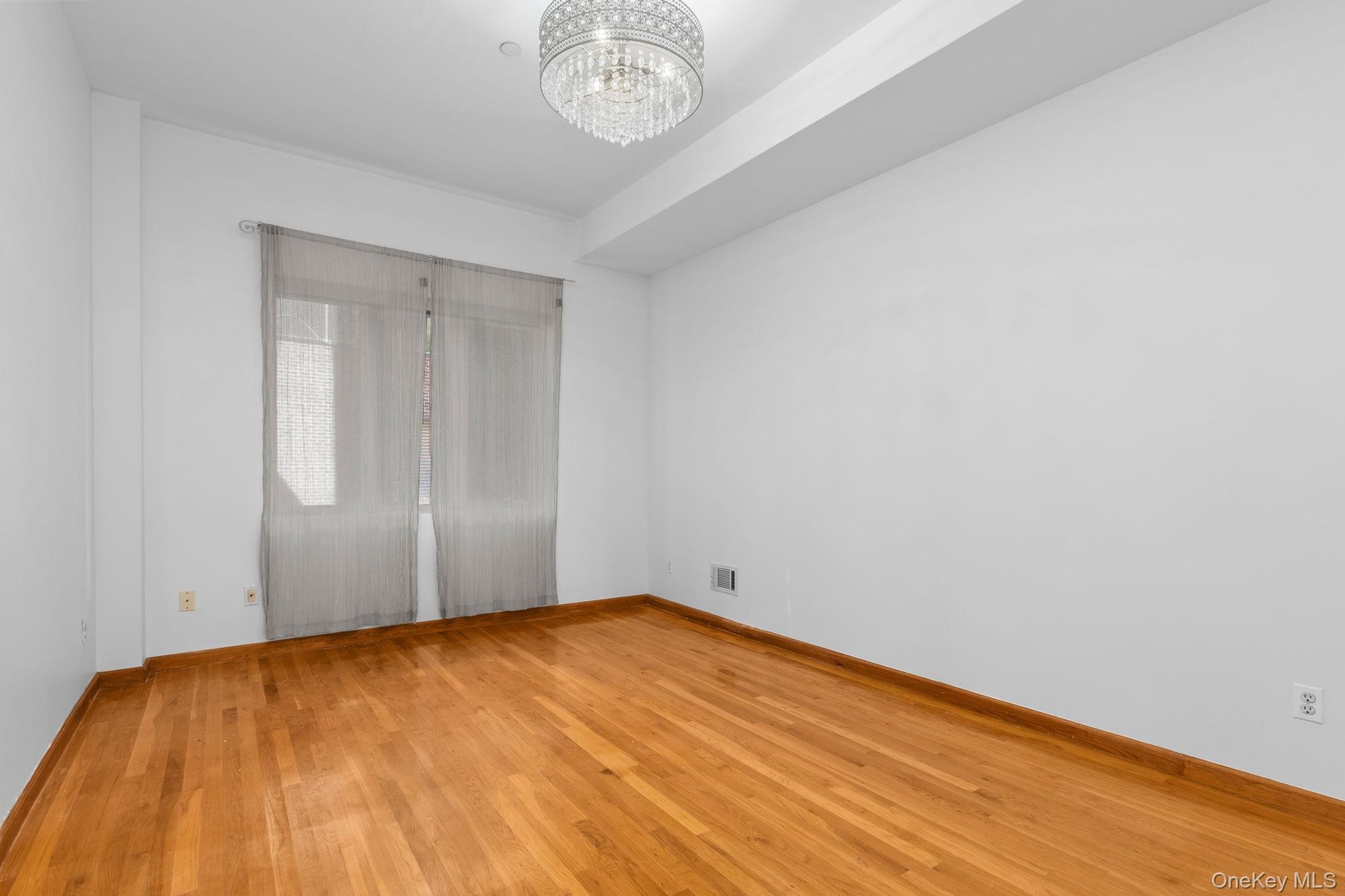Primary bedroom featuring wood-finish flooring, a decorative crystal-style chandelier, and a recessed ceiling design.