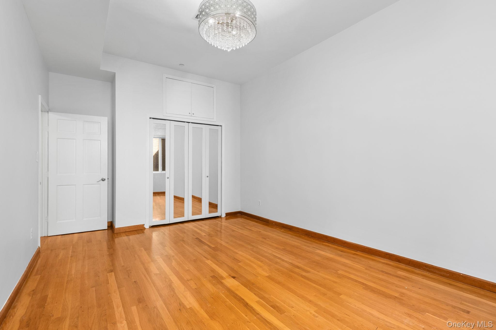 Wood-finish flooring, mirrored closet doors, overhead crystal-style chandelier, and built-in upper storage cabinetry.