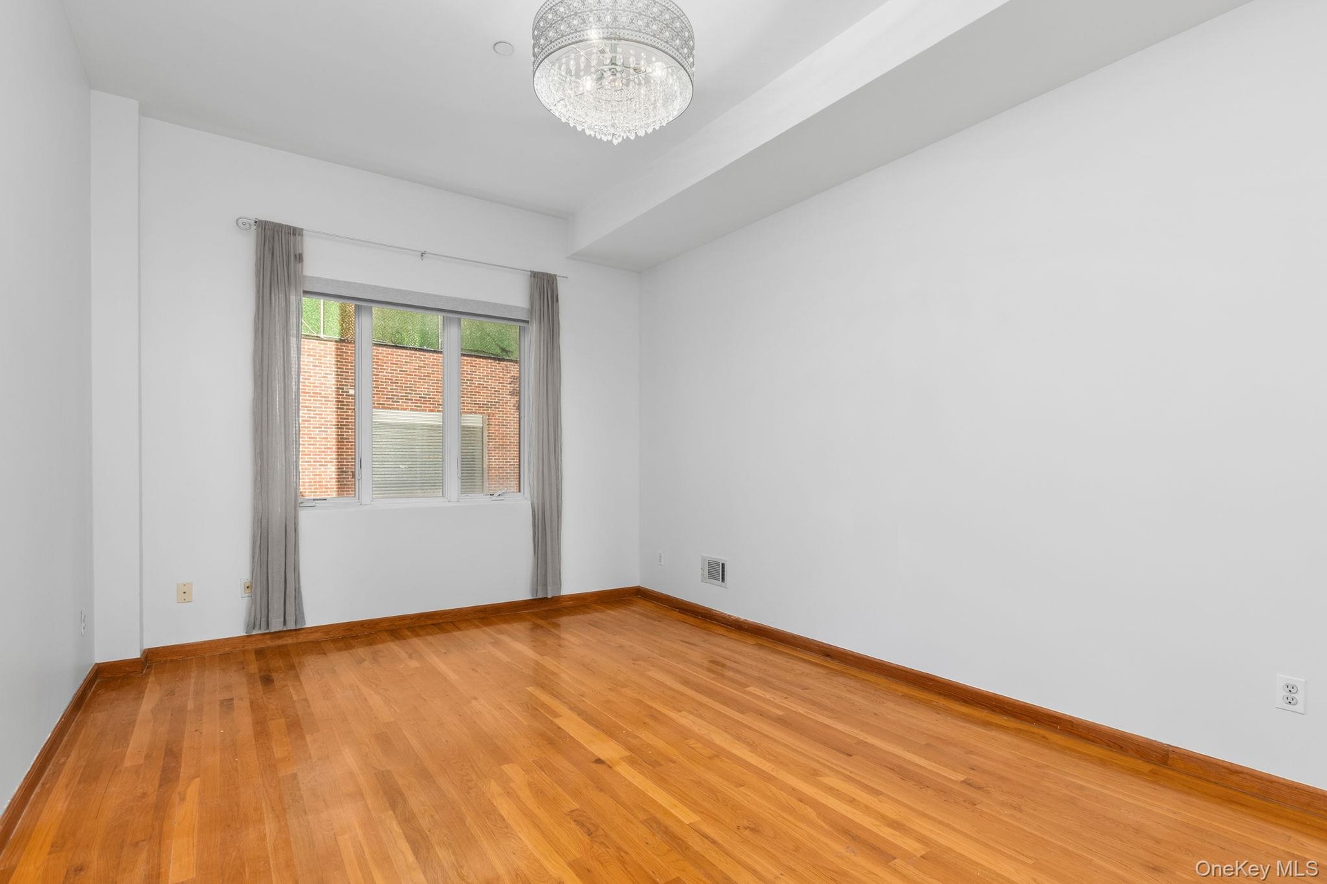 Primary bedroom featuring wood-finish flooring, a tiered ceiling, and a multi-tiered crystal chandelier fixture.