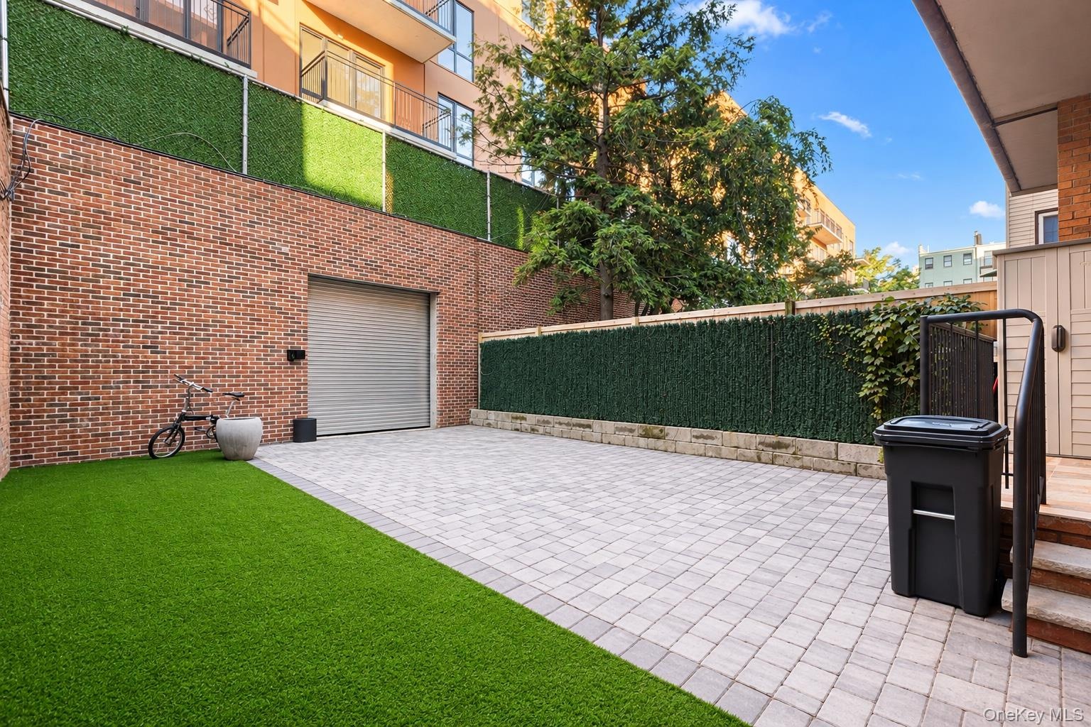 Private outdoor patio featuring brick wall construction, synthetic turf, stone paver hardscaping, with a detached garage for private parking and perim