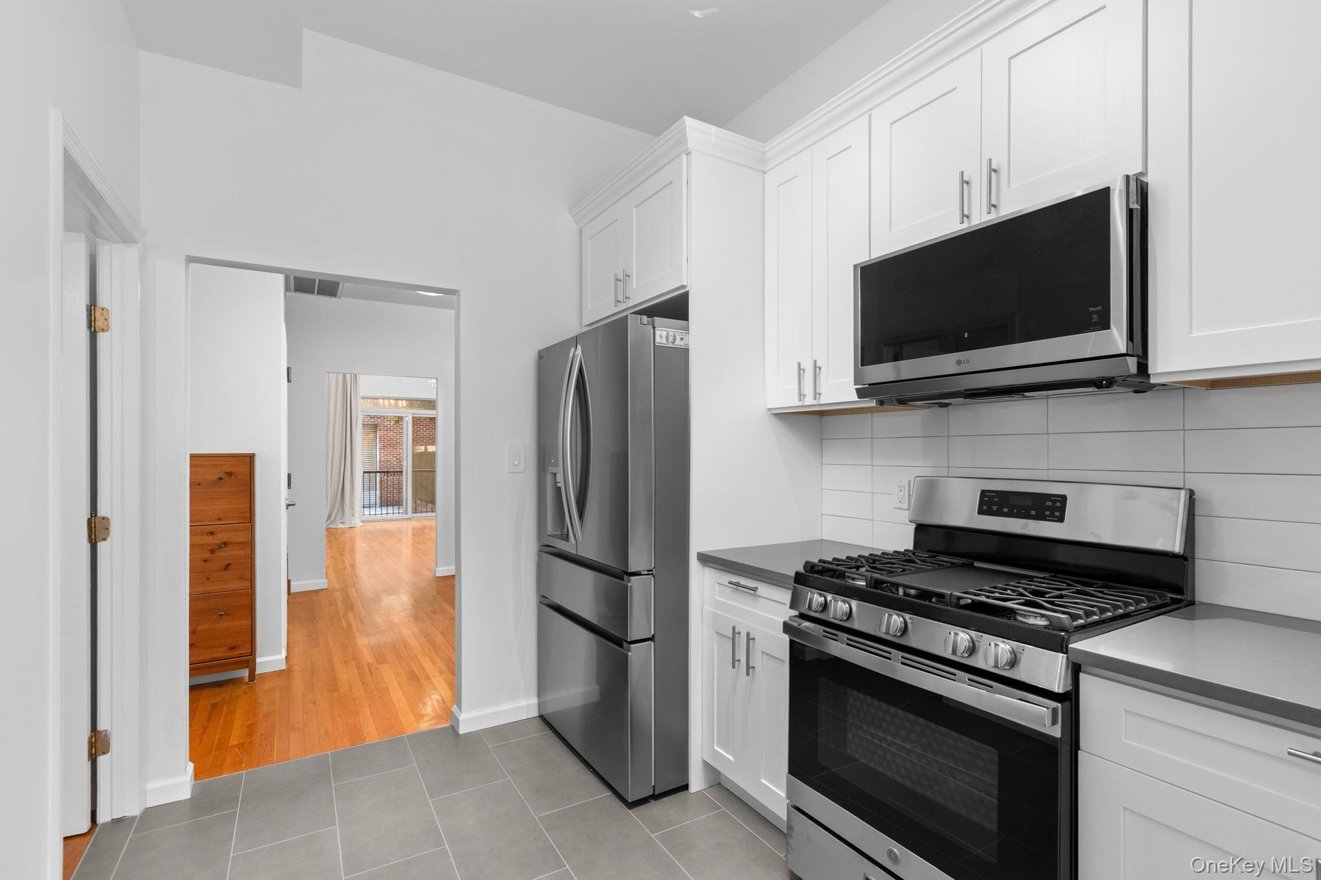 Kitchen featuring white shaker-style cabinetry, stainless steel appliances, a gas range with an over-the-range microwave, solid-surface countertops, a