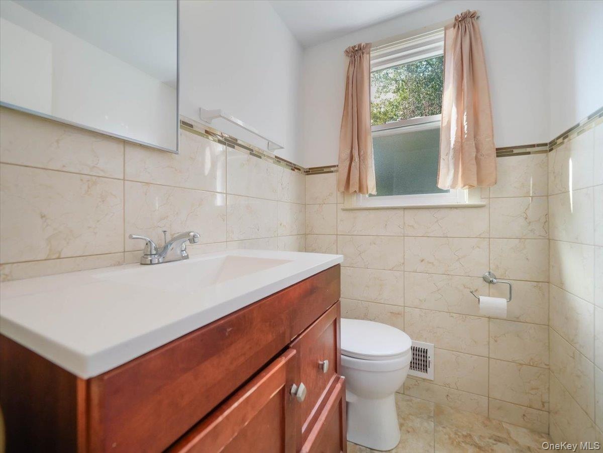 Bathroom featuring a wood-finish vanity with a white integrated sink, full-height wall tiling with a mosaic accent border, and a large wall-mounted mi