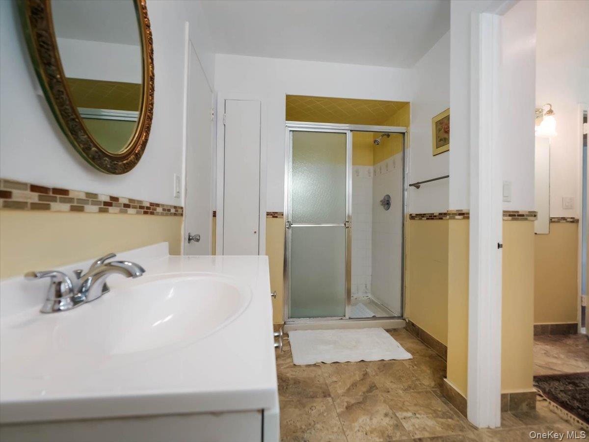 Bathroom featuring a vanity with a white integrated sink, walk-in shower with a sliding glass door, decorative tile backsplash, and tile flooring