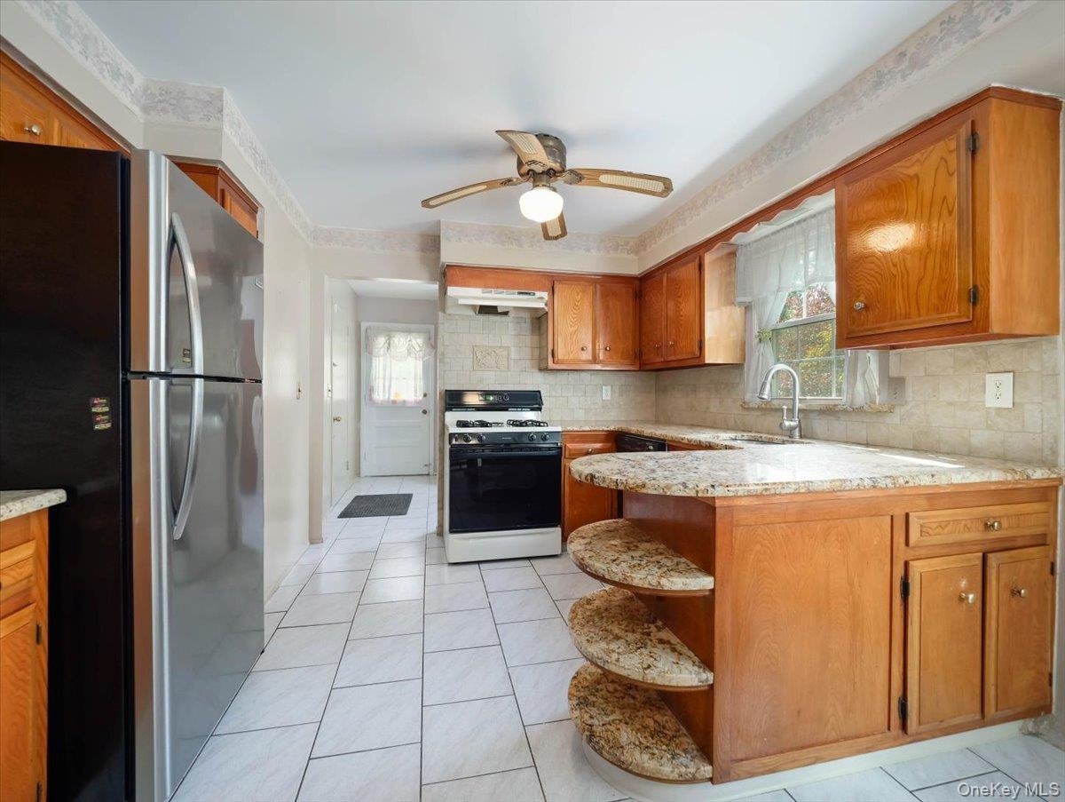 Kitchen featuring wood cabinetry, natural stone countertops with integrated open shelving, tile flooring, and stainless steel appliances