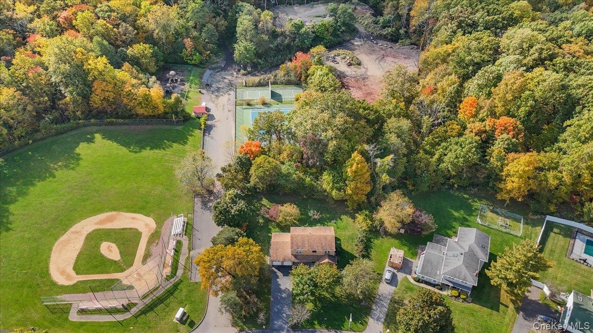 Aerial perspective featuring expansive green space, mature deciduous trees, a baseball diamond, and a tennis court