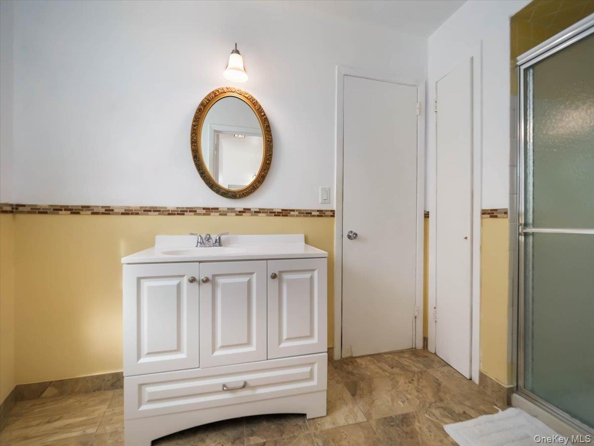 White vanity with integrated sink, stone-finish tile flooring, walk-in shower enclosure, and decorative tile backsplash