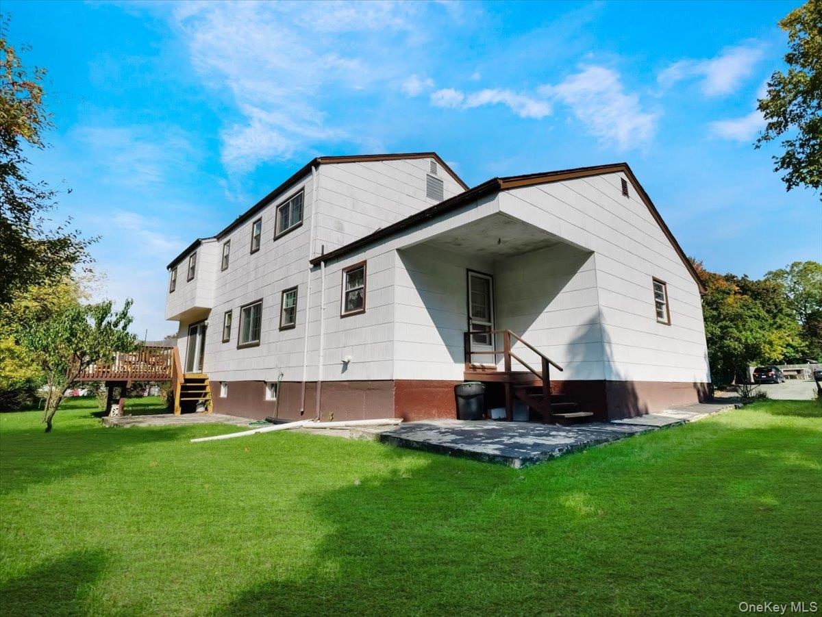 Exterior featuring a two-story structure with a concrete patio, elevated wooden deck, stairs, and a level lawn
