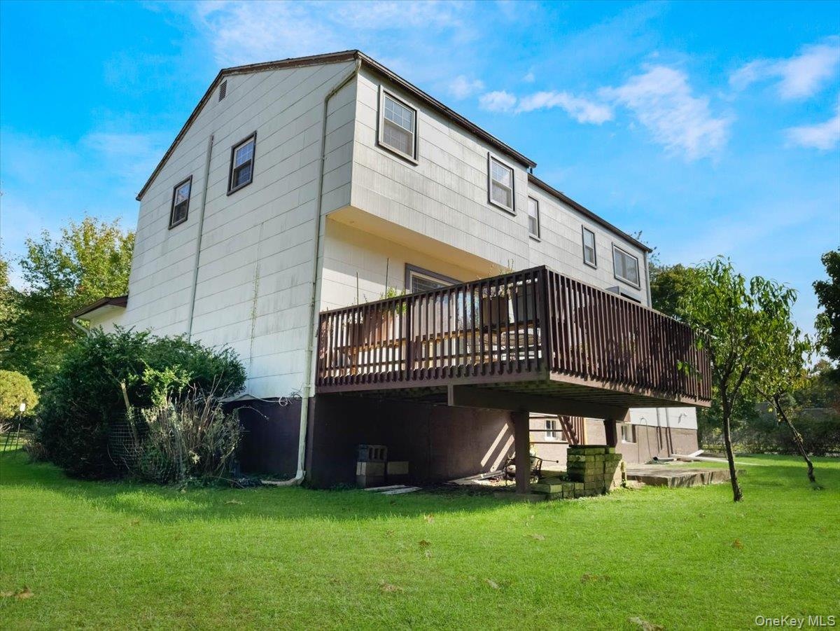 Rear exterior featuring vertical siding, a raised wood deck with balustrades, a stone retaining wall, and a large grassy lot