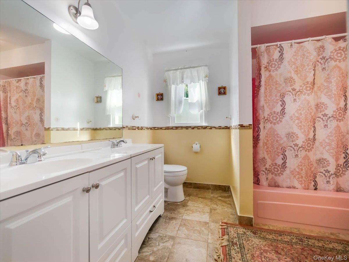 Dual-sink vanity with white cabinetry, oversized wall-mounted mirror, mosaic tile backsplash, and stone-finish flooring