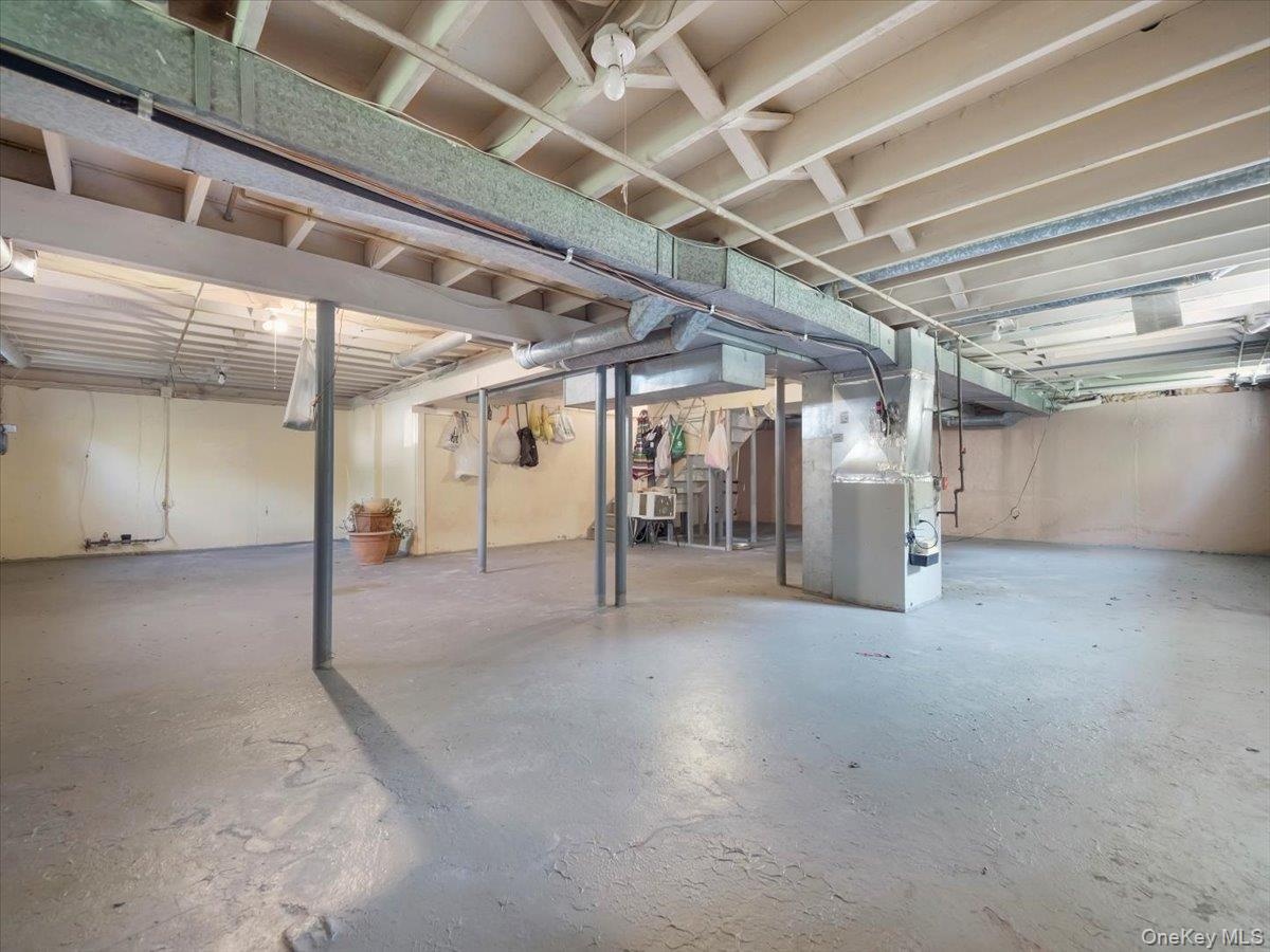 Unfinished basement featuring exposed structural ceiling joists, painted concrete flooring, and metal support columns