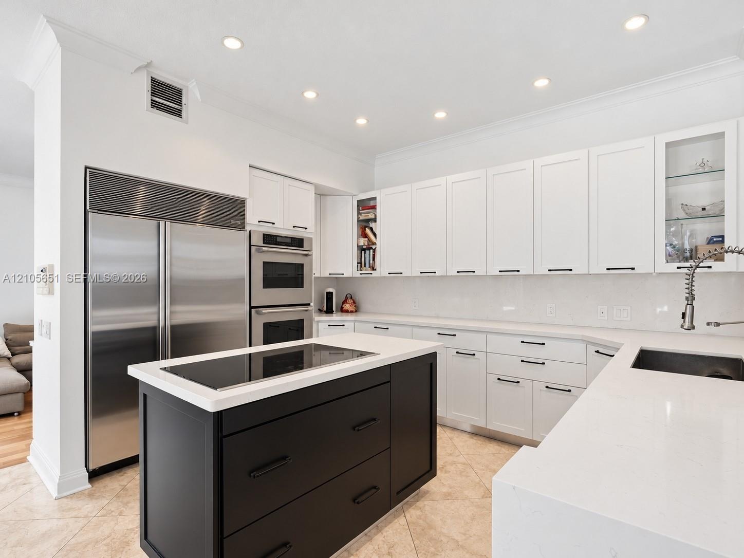 Kitchen featuring white shaker-style cabinetry, contrasting black center island, built-in stainless steel double wall oven, integrated refrigerator, a