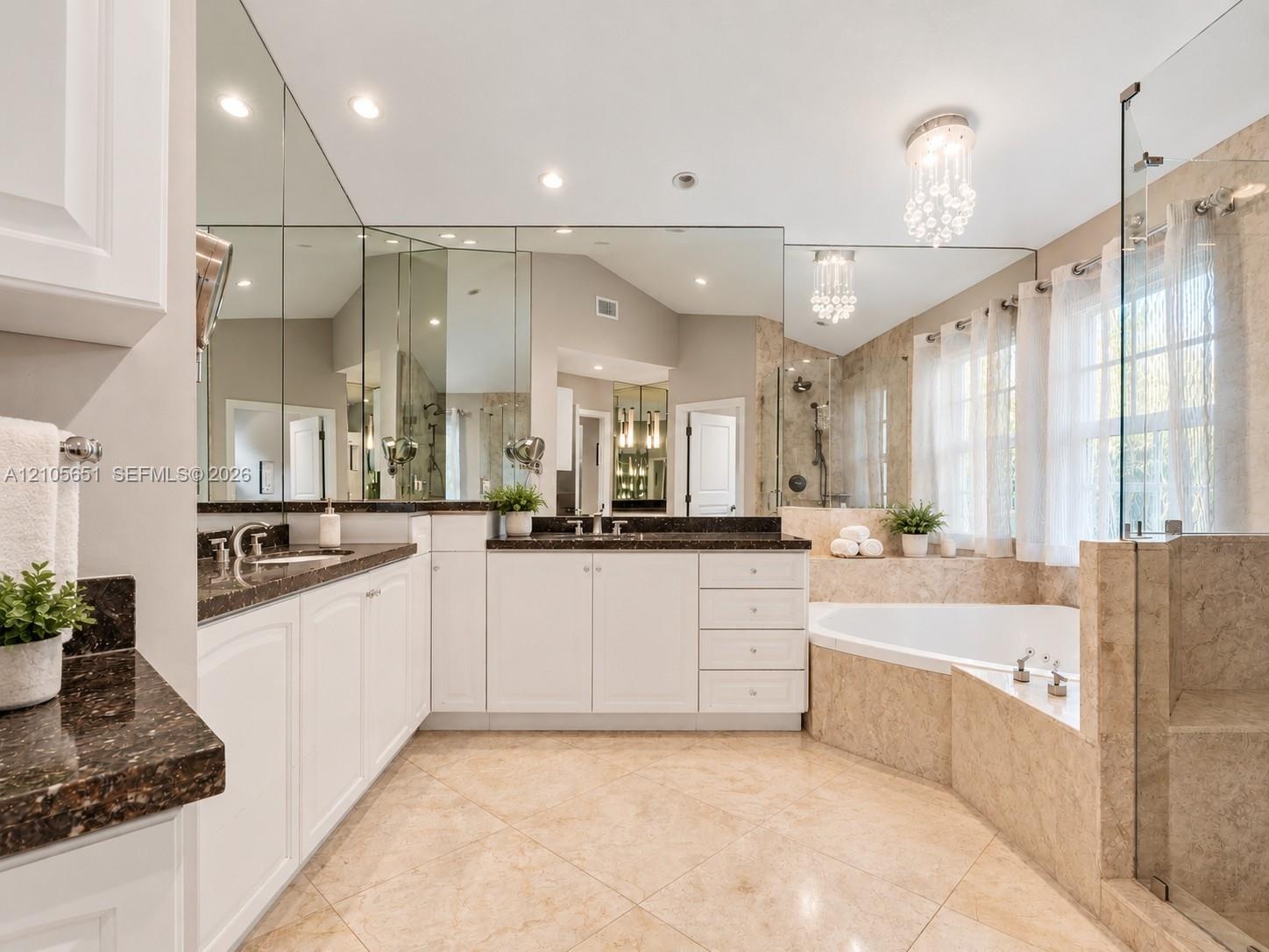 Bathroom featuring a double vanity with stone countertops, tiled soaking tub, walk-in glass-enclosed shower, wall-to-wall mirrors, and crystal light f