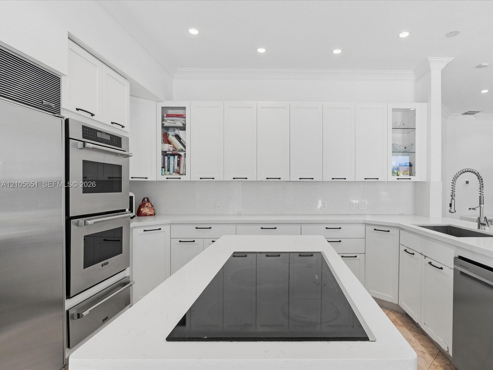 Kitchen featuring white cabinetry with glass-front display panels, quartz countertops, a central island with an integrated cooktop, double wall ovens,