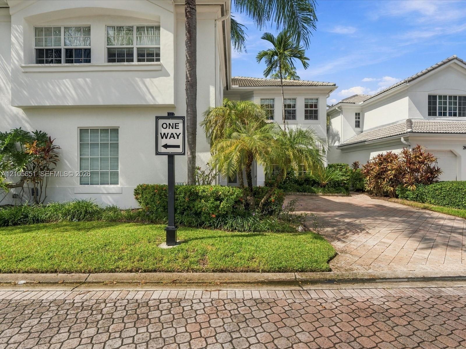 Stucco exterior featuring multi-pane windows, a tiled roof, and a paved brick driveway