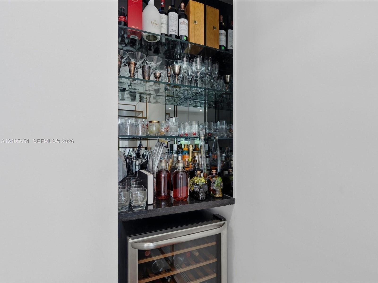 Built-in recessed display cabinet featuring mirrored backing, glass shelving, a dark stone countertop, and an integrated stainless steel wine refriger