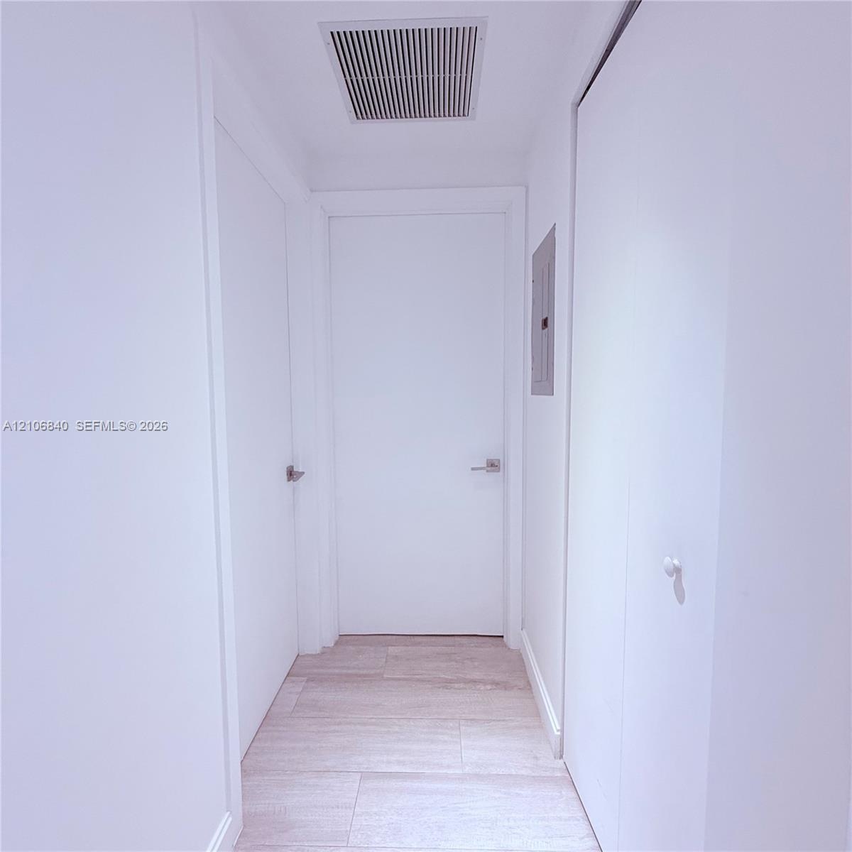 Hallway featuring light-toned wood-finish flooring, solid-core doors with brushed metal lever handles, and neutral wall finishes