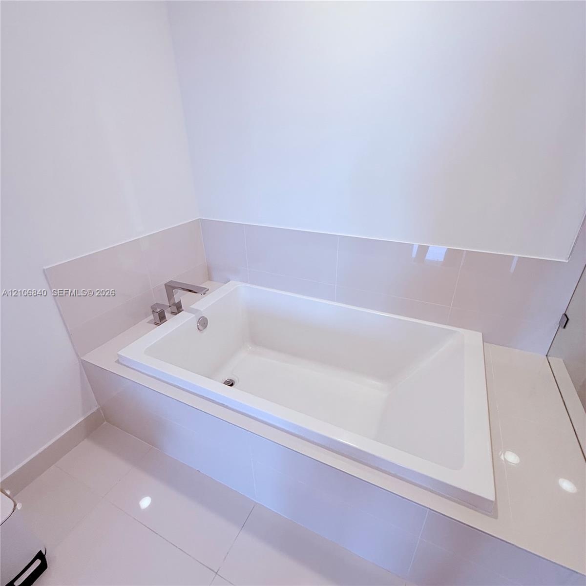 Built-in soaking tub with a chrome deck-mounted faucet and surround finished in large-format neutral tile
