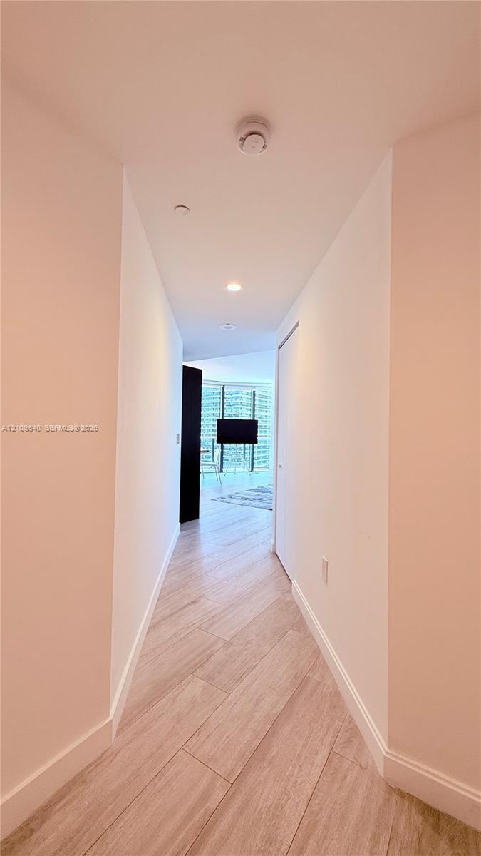 Hallway featuring neutral-toned walls, wood-finish tile flooring, and recessed ceiling lighting