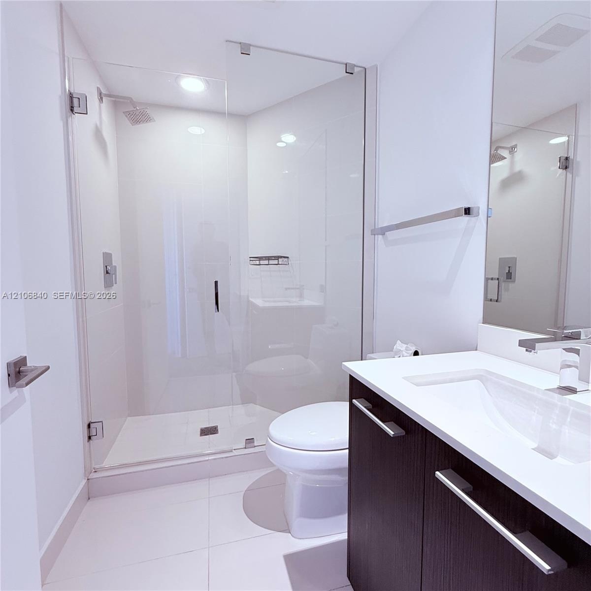 Walk-in shower with frameless glass enclosure, dark-finish cabinetry, solid-surface vanity countertop with integrated sink, polished chrome faucet, an