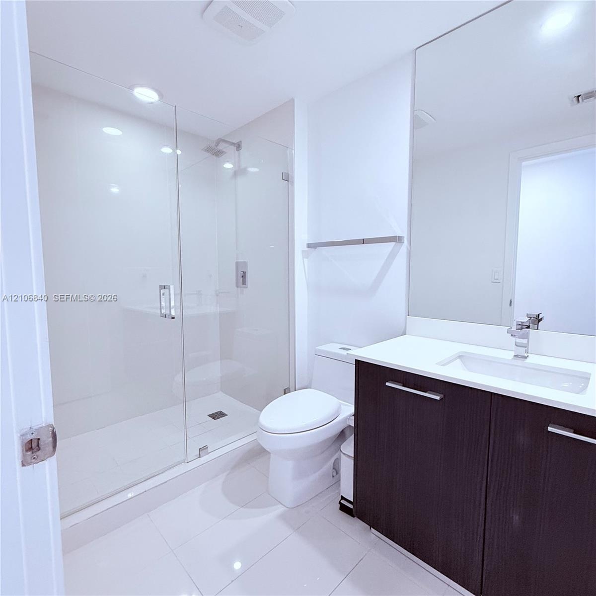 Bathroom featuring a glass-enclosed walk-in shower, dark-toned vanity with a light-colored countertop, integrated rectangular sink, and floor-to-ceili