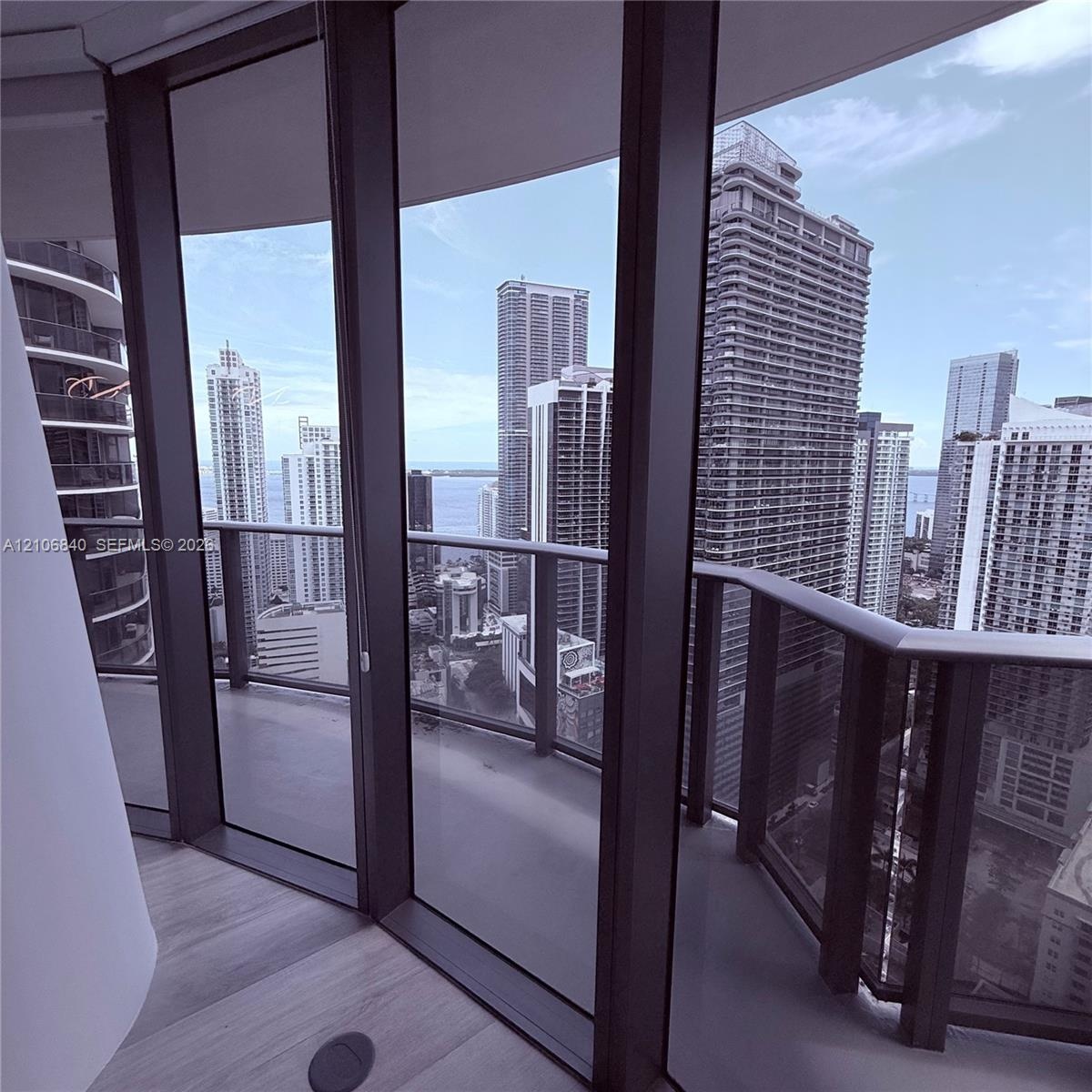 Floor-to-ceiling glass paneling, wraparound balcony with metal railings, and wood-finish flooring
