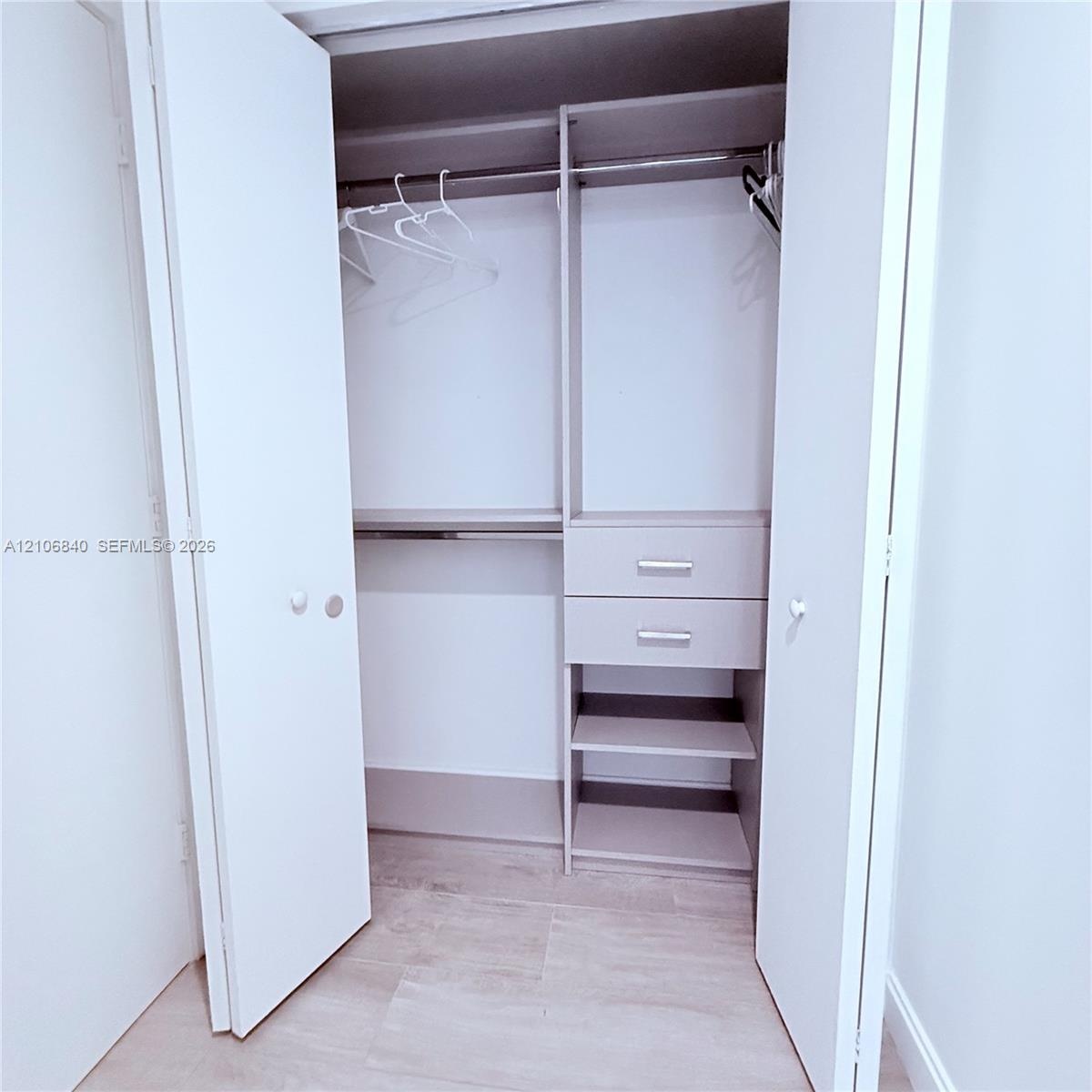 Closet featuring bi-fold doors, integrated shelving, two storage drawers with metallic hardware, and a metal hanging rod