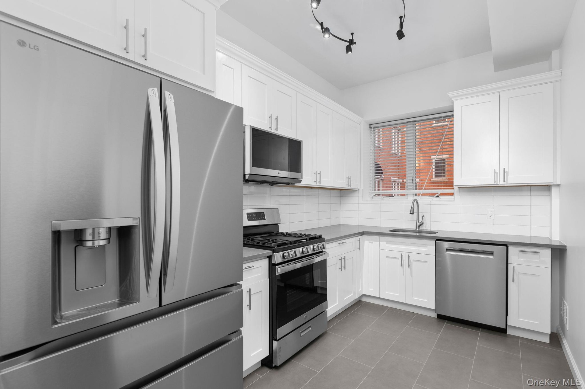 Kitchen featuring white shaker-style cabinetry, solid-surface countertops, subway tile backsplash, stainless steel appliances, and large-format tile f