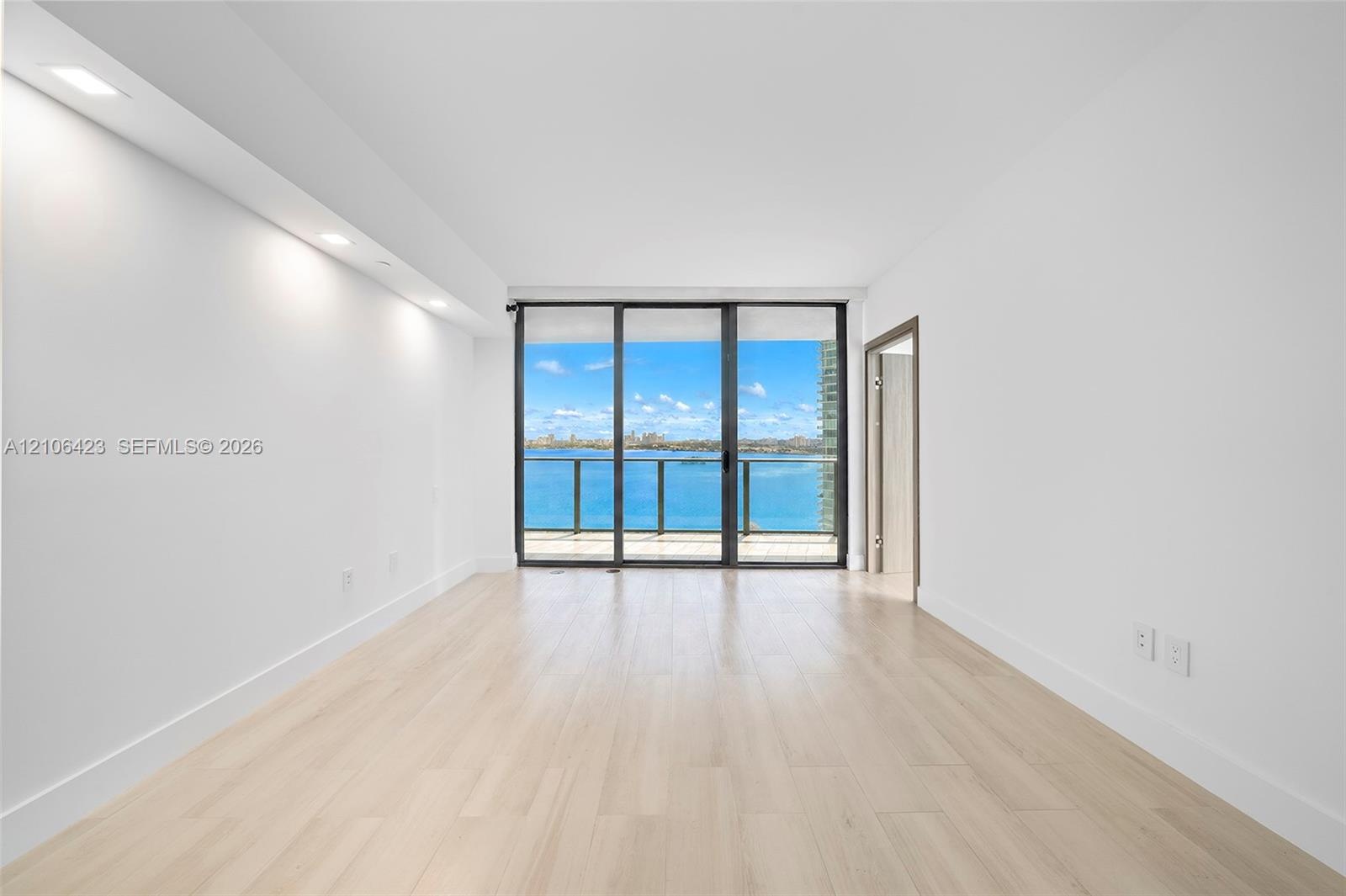 Interior space featuring light-toned wood-finish flooring, recessed ceiling lighting, and floor-to-ceiling glass sliding doors opening to an exterior 