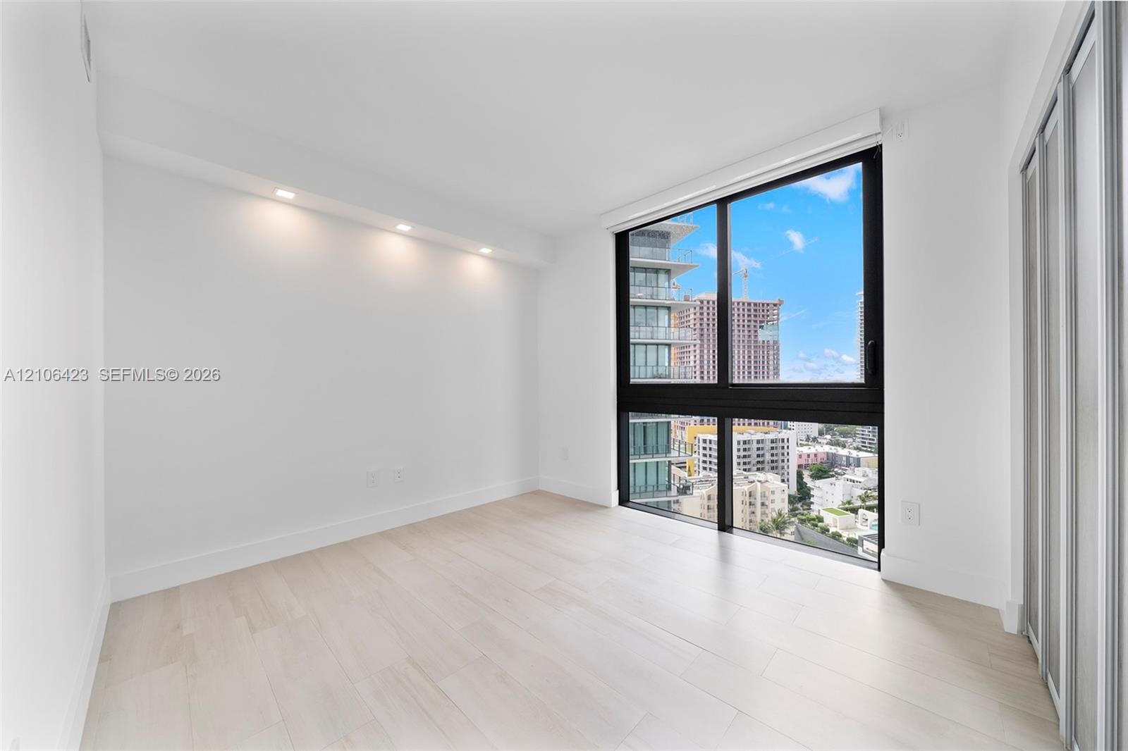 Light-filled room featuring floor-to-ceiling windows with black frames, wood-finish flooring, recessed architectural lighting, and floor-to-ceiling sl