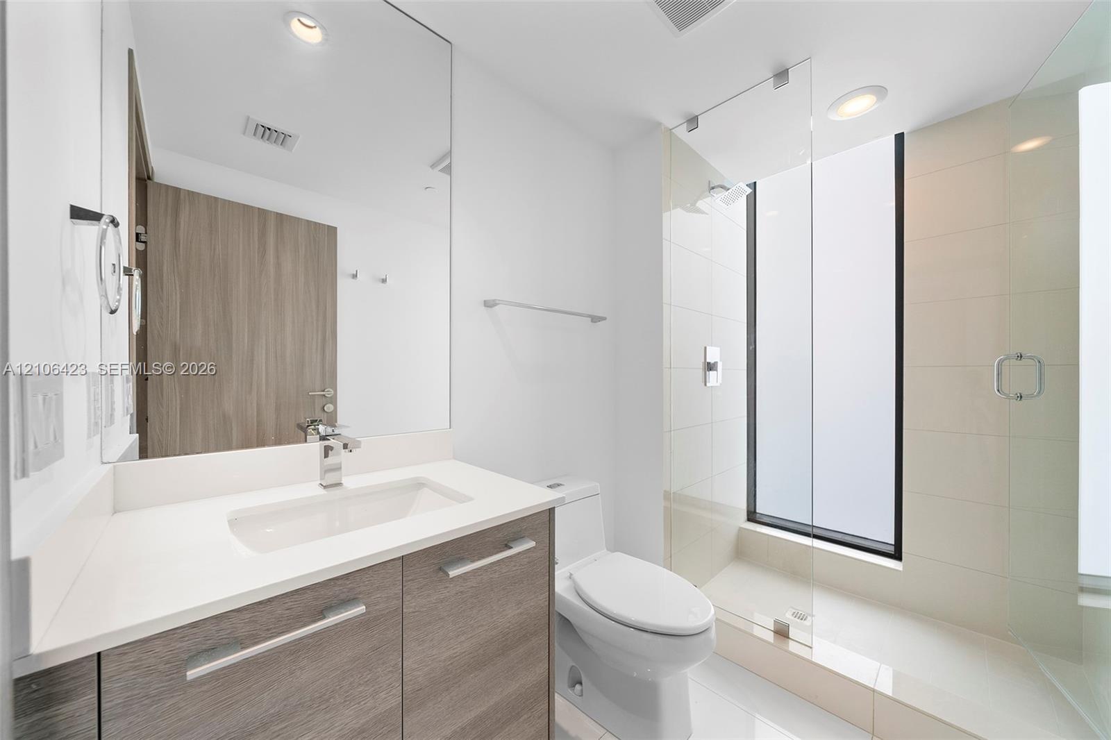Bathroom featuring a floating wood-finish vanity with a white countertop, large frameless mirror, glass-enclosed walk-in shower with floor-to-ceiling 