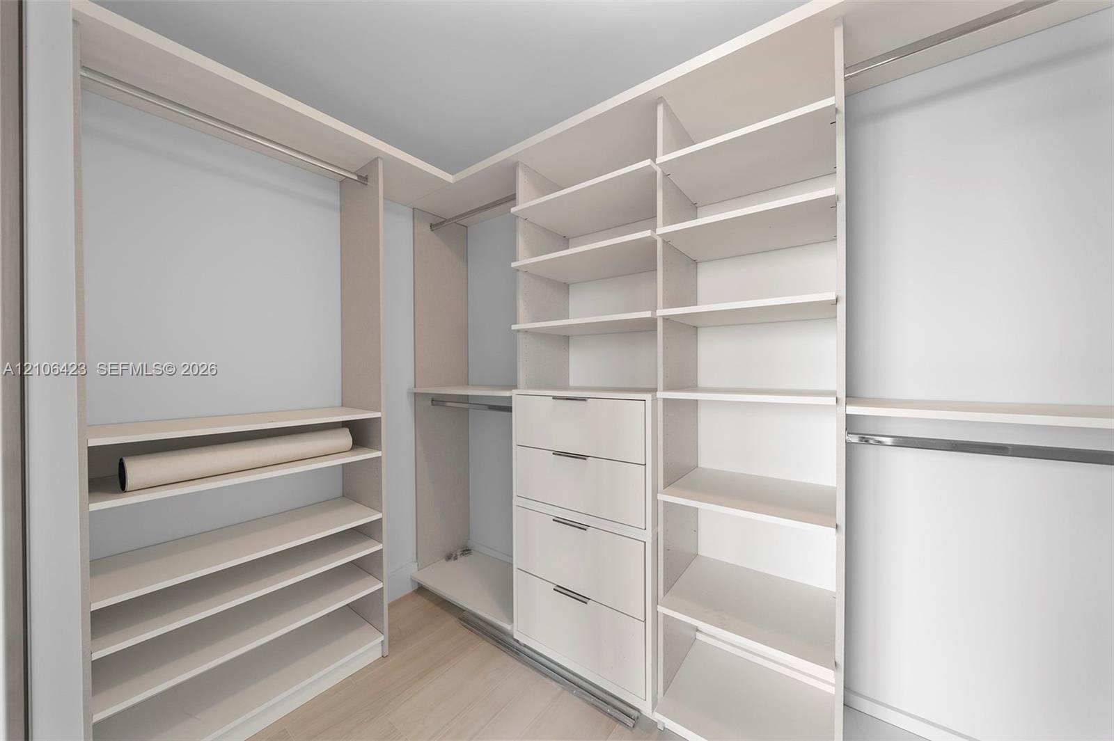 Custom walk-in closet featuring light-toned built-in cabinetry, floor-to-ceiling shelving, integrated hanging rods, and a multi-drawer dresser unit