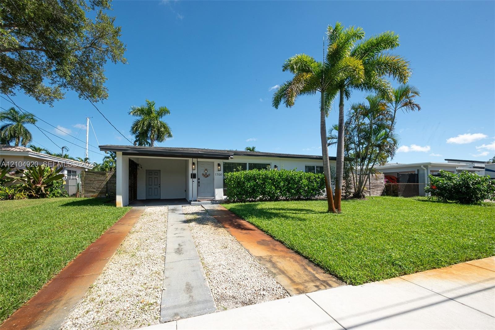 Single-story residence featuring a covered carport, concrete driveway, mature palm trees, and established landscaping