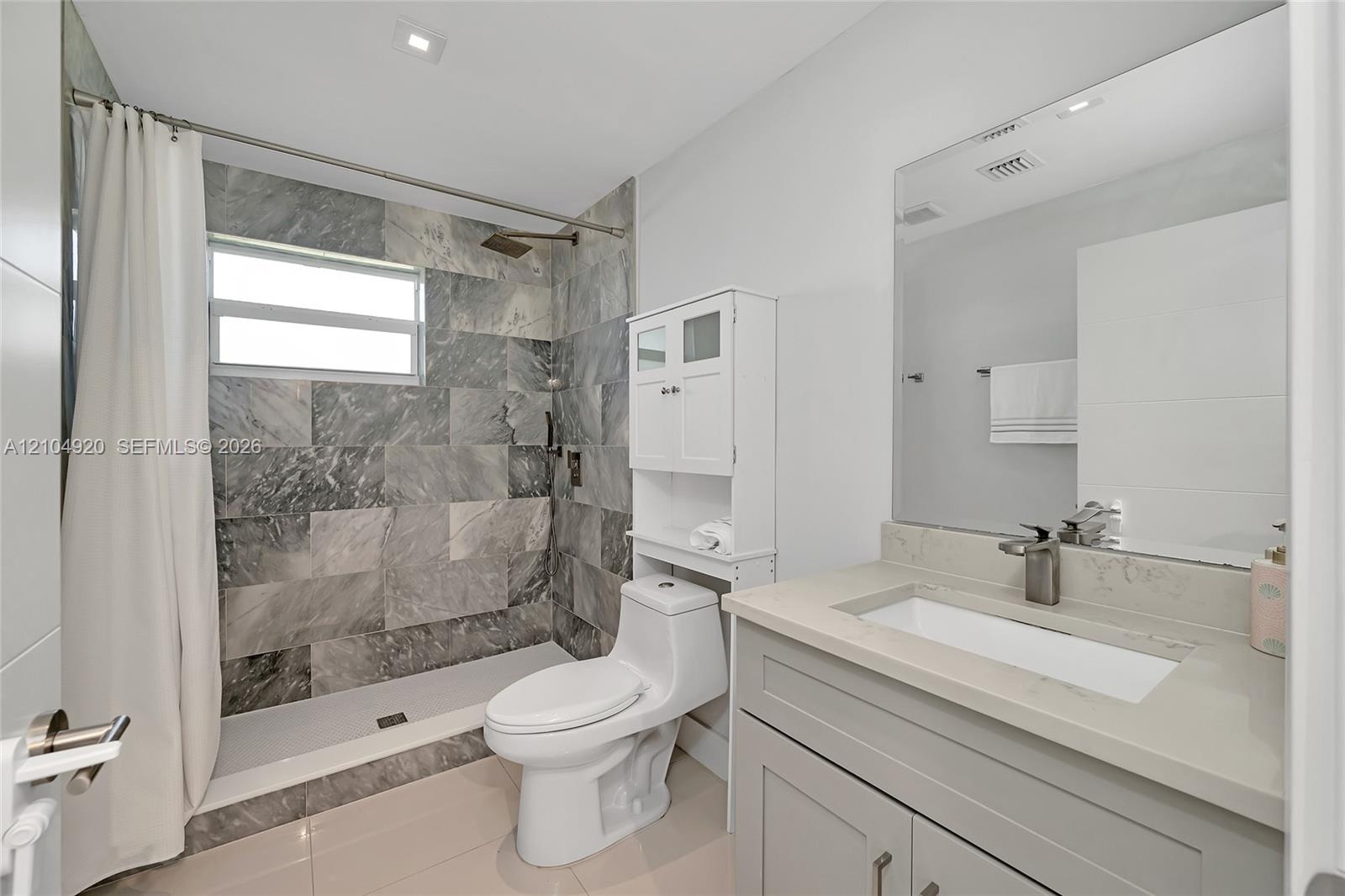 Full-height shower enclosure featuring stone-tiled walls and an overhead rain showerhead, complemented by a stone-topped vanity with an integrated bas
