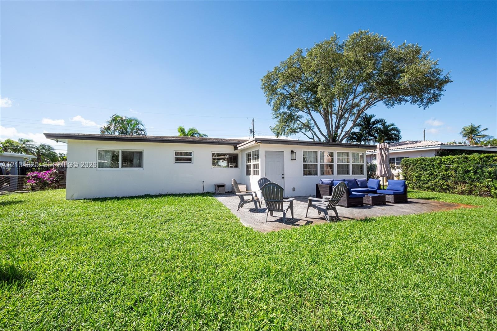 Rear exterior featuring a concrete patio, white stucco siding, multi-pane windows, and a mature tree providing canopy