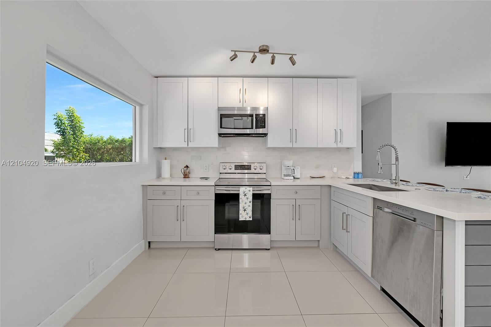 Kitchen featuring shaker-style cabinetry, stainless steel appliances, light-toned stone-finish countertops, tile flooring, and multi-directional track