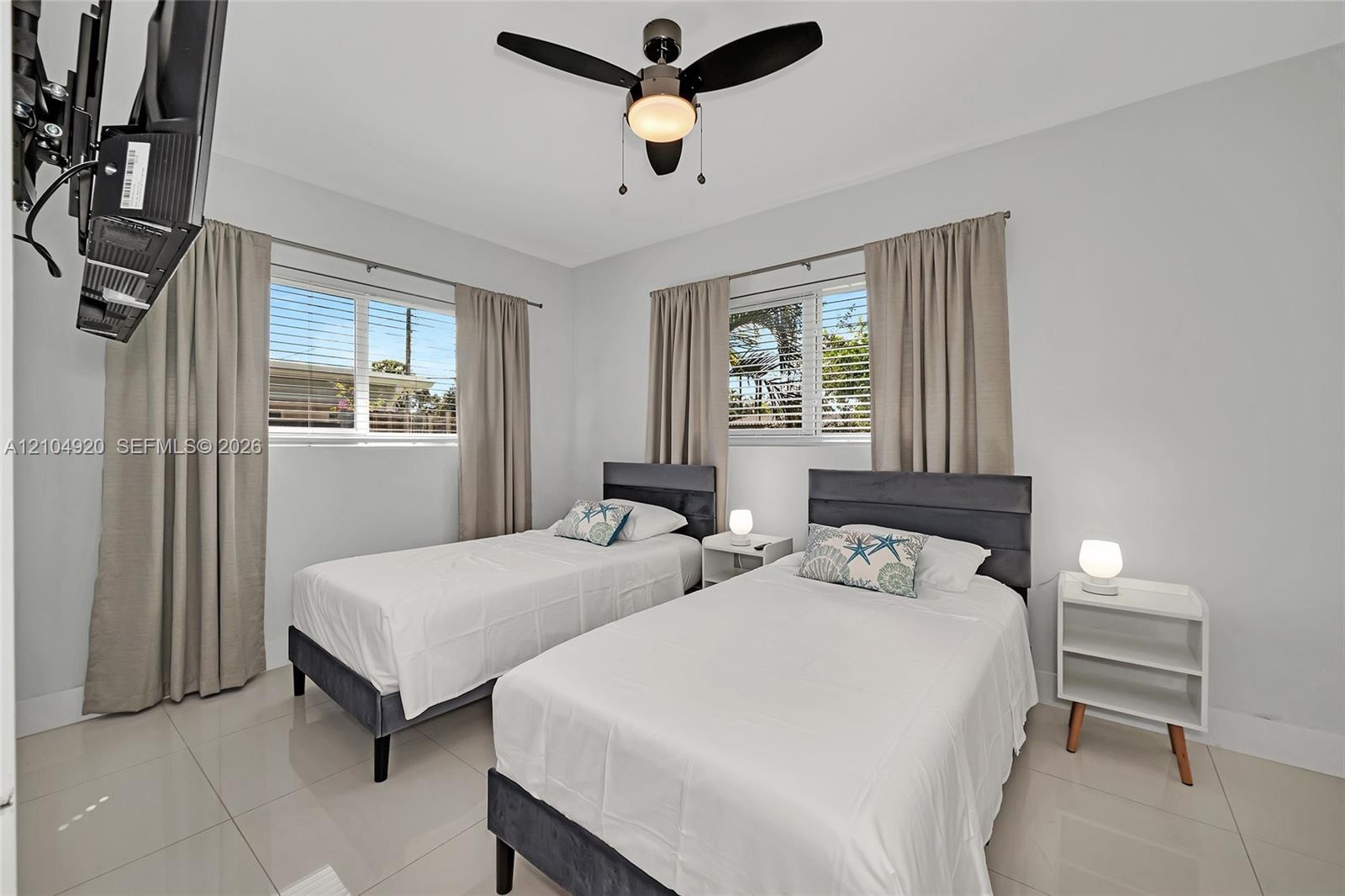 Neutral-toned interior space featuring light-colored tile flooring, multiple windows with horizontal blinds, and a contemporary ceiling fan with integ