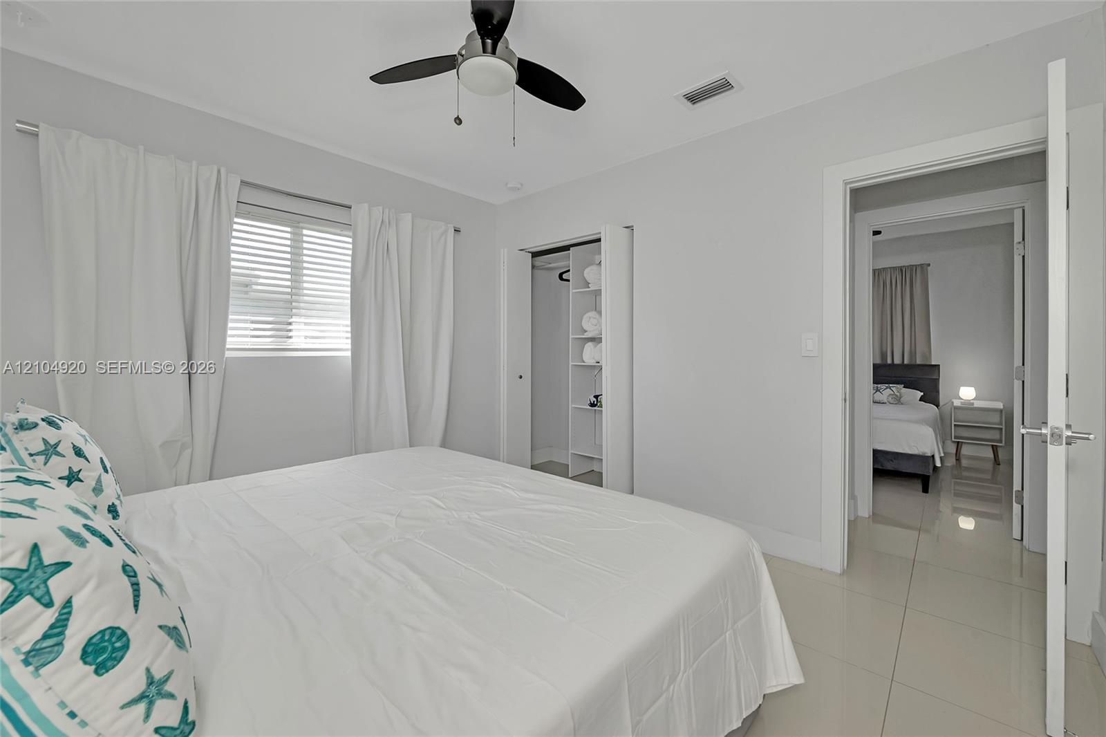 Neutral-toned interior featuring oversized tile flooring, a ceiling fan with integrated lighting, a built-in closet shelving system, and horizontal wi