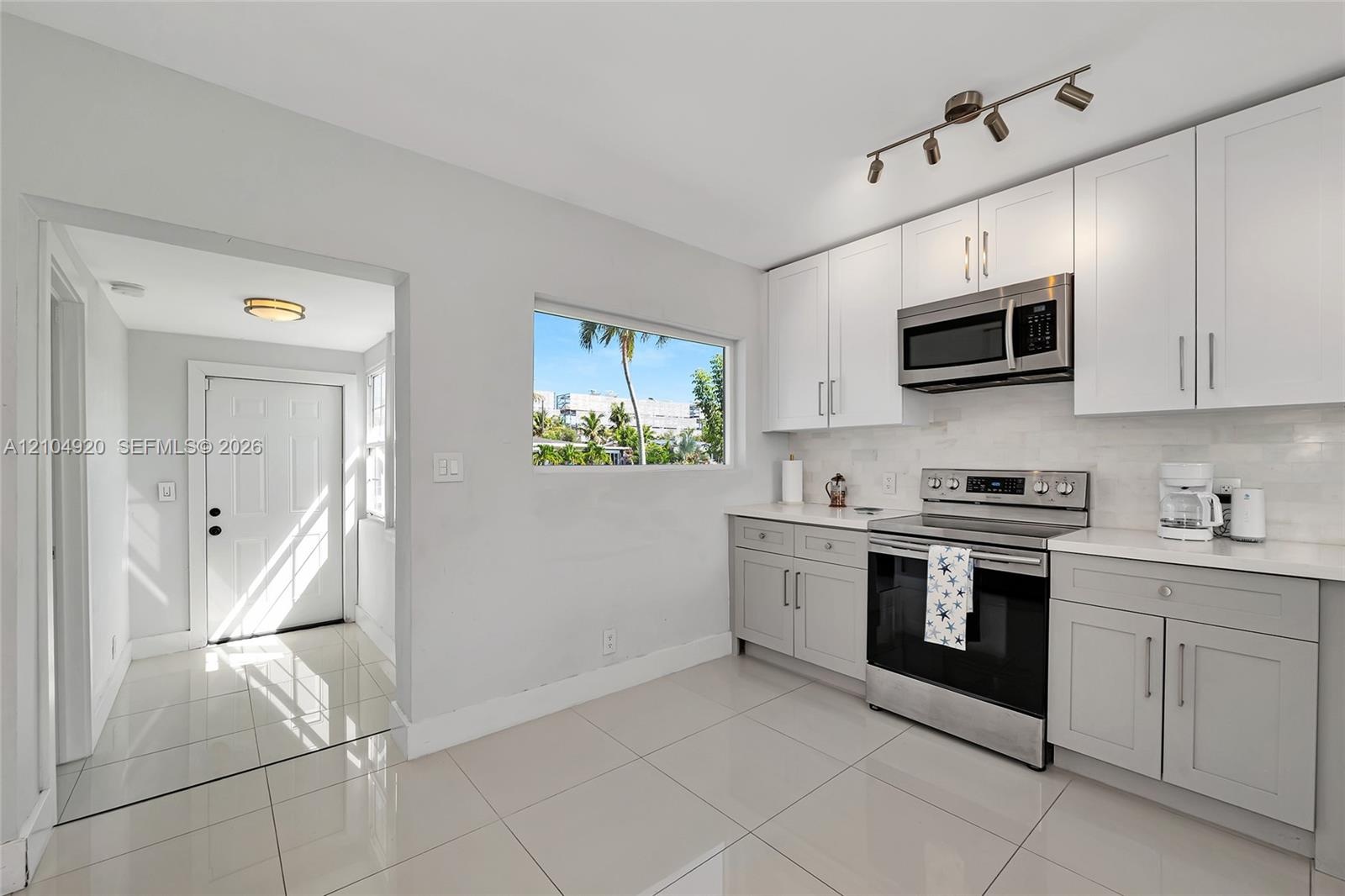 Kitchen featuring white and grey shaker-style cabinetry, stainless steel appliances, polished stone-finish tile flooring, and track lighting